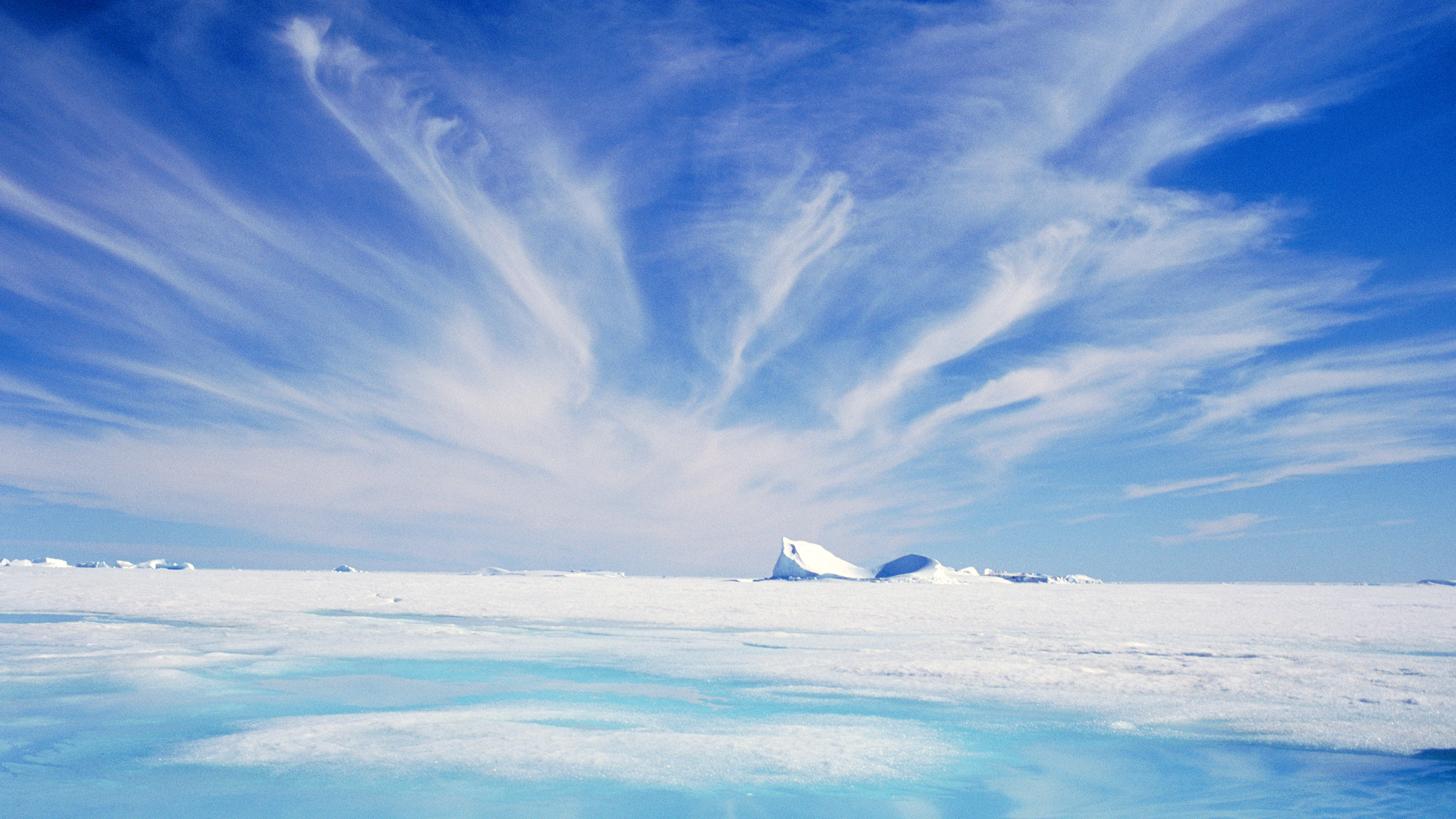 Photograph showing cirrus clouds in a blue sky above an expanse of flat, snow-covered ice.