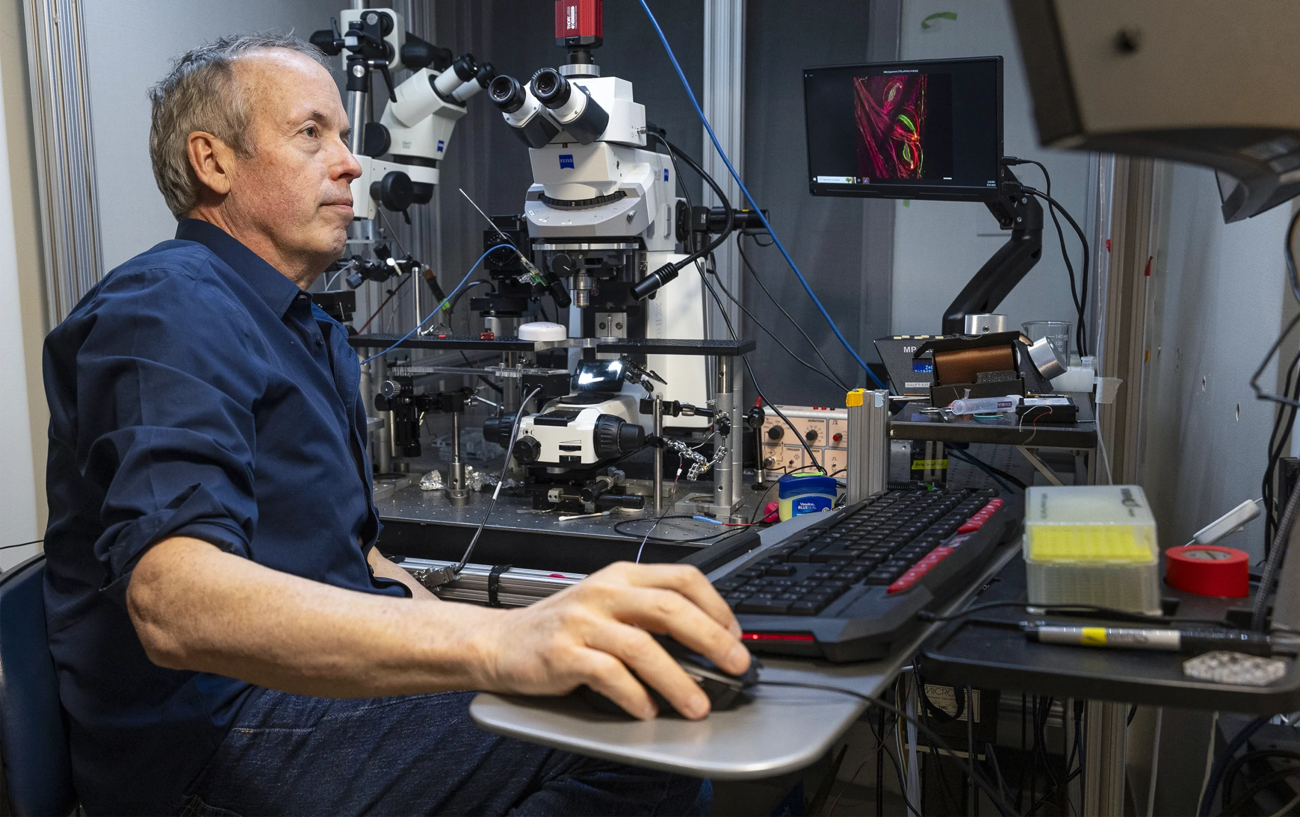 Ginty sits at a computer near two microscopes.